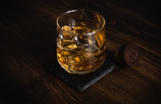 Glass of whiskey with ice on a wooden table representing distillery tasting experience