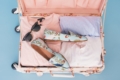Packed suitcase with summer clothes, shoes, and sunglasses for a beach vacation.
